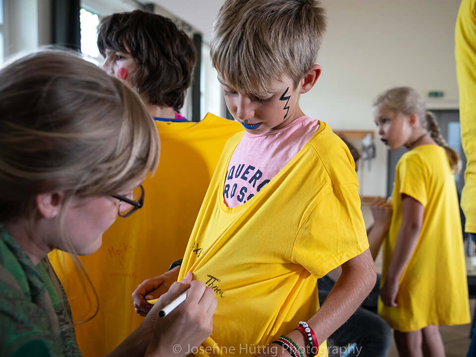 Theatervermittlungsprogramm Theater begegnen, Frau malt einem Jungen auf das gelbe Tshirt