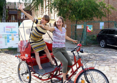 zwei Frauen in der Fahrradrikscha, die Arme von sich gestreckt